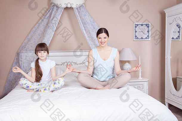 快乐妈妈。女儿冥想微笑坐着瑜伽构成床上首页工作室拍摄