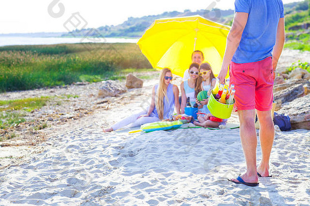 朋友坐着沙子海滩夏天野餐男人。持有绿色桶柠檬水关闭