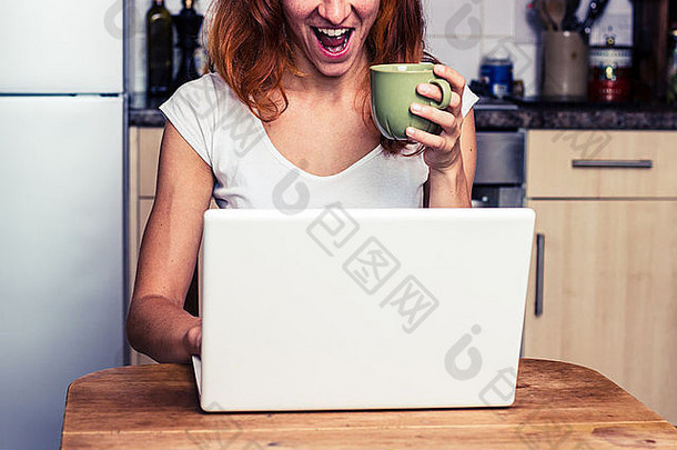 快乐年轻的女人喝咖啡移动PC厨房
