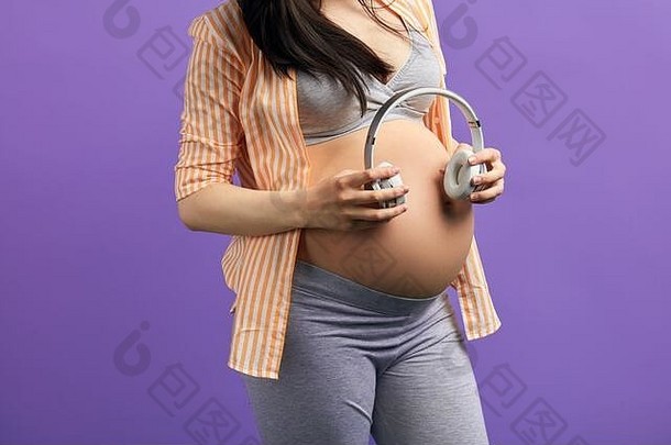 特写镜头怀孕了高加索人女人长黑暗头发把耳机腹部订单未出生的婴儿听到自然听起来