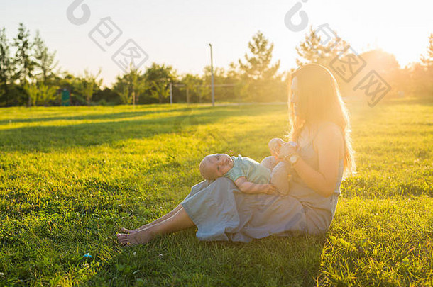 年轻的女人男孩草地阳光明媚的一天快乐家庭夏天日落妈妈。婴儿