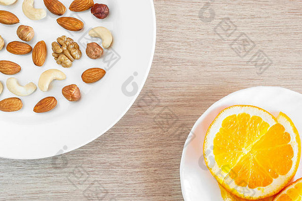 各种各样的坚果橙色片白色盘子木表格健康的有机零食早餐食物成分平躺自顶向下作文
